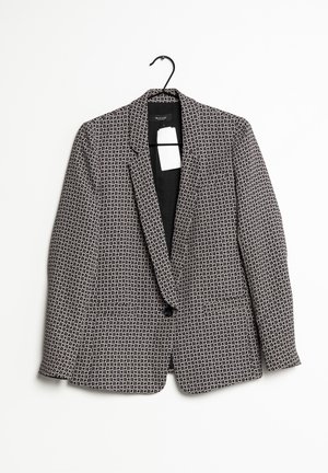 Zwart-wit geruite blazer met één knoop, hangend aan een zwarte hanger tegen een effen witte achtergrond.