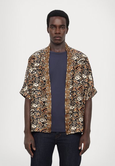 Kimono stylová košile s černým a zlatým vzorem, volnými rukávy a kontrastním lemem. Nosená přes námořnickou modrou tričko a tmavé džíny.