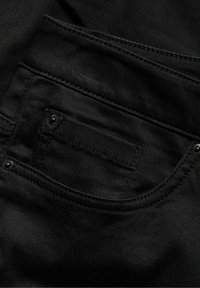 Svart denimtyg med en liten framficka med synliga sömmar och svarta metalldetaljer. Slät textur med minimal lyster.