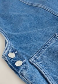 Gros plan sur un tissu en jean bleu avec deux boutons métalliques argentés et un détail de poche cousu.