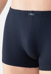 Nærbillede af en person iført mørkeblå tætsiddende boxershorts med et lille "mey"-mærke på elastikken.