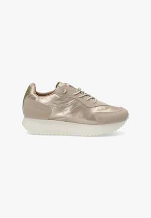 Zapatilla deportiva de color beige claro con parte superior sintética brillante, acentos de ante y parte trasera texturizada. Presenta suela de goma blanca y diseño de cordones.