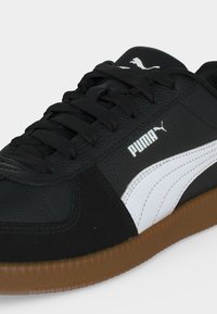 Μαύρο αθλητικό παπούτσι Puma με λευκή πλαϊνή ρίγα, λαστιχένια σόλα, μαύρα κορδόνια και λογότυπο Puma στο πλάι και στη γλώσσα.