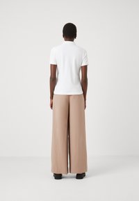 Polo shirt bianco con maniche corte abbinato a pantaloni larghi color marrone chiaro. Tessuto liscio, design minimalista e vestibilità rilassata.