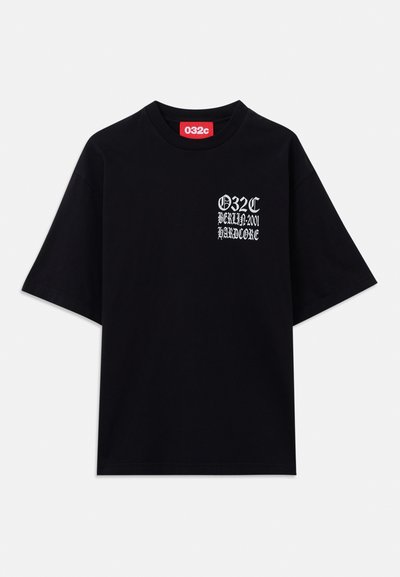 T-shirt noir surdimensionné en coton. Il comporte un imprimé graphique blanc sur le côté gauche avec le texte "032C BERLIN 2001 HARDCORE."
