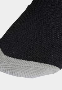 Calcetín negro de punto con un puño acanalado gris y superficie texturada. Las áreas del talón y la puntera están reforzadas para mayor durabilidad.