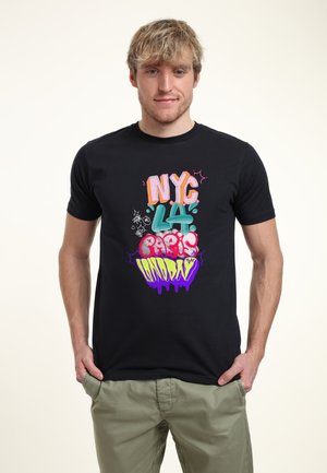 Zwarte T-shirt met kleurrijke graffiti-stijl tekst: "NYC LA Parijs Maandag" met spatten en druppels in roze, groen en paars.