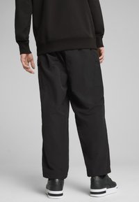 Czarne, oversize'owe spodnie o teksturowanym wykończeniu, z bocznymi kieszeniami i luźnym krojem, w połączeniu z czarnymi trampkami z białymi podeszwami.
