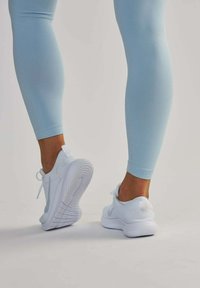Białe sportowe buty z teksturowanym siateczkowym wierzchem i gumową podeszwą, w połączeniu z dopasowanymi jasnoniebieskimi legginsami. Minimalistyczny design z subtelnym logo.