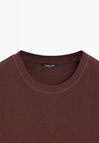 Bruin T-shirt met een ronde hals en zichtbare stiksels rondom de kraag, met een zwart Massimo Dutti-label genaaid aan de binnenkant van de halslijn.