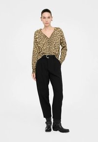Bluse med leopardprint, v-hals og knaplukning, kombineret med højtaljede sorte bukser og ankelstøvler med pynt.