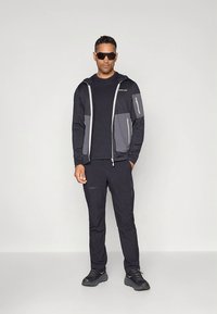 Moška športna obleka z črno jakno na zadrgo s kapuco in sivimi poudarki ter ujemajočimi se črnimi hlačami, izdelana iz lahkega in zračnega materiala.