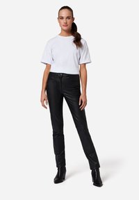 Svarta läderbyxor i slim-fit med en slät yta, kombinerade med en vit kortärmad t-shirt. Modellen bär svarta klackade ankelstövlar.