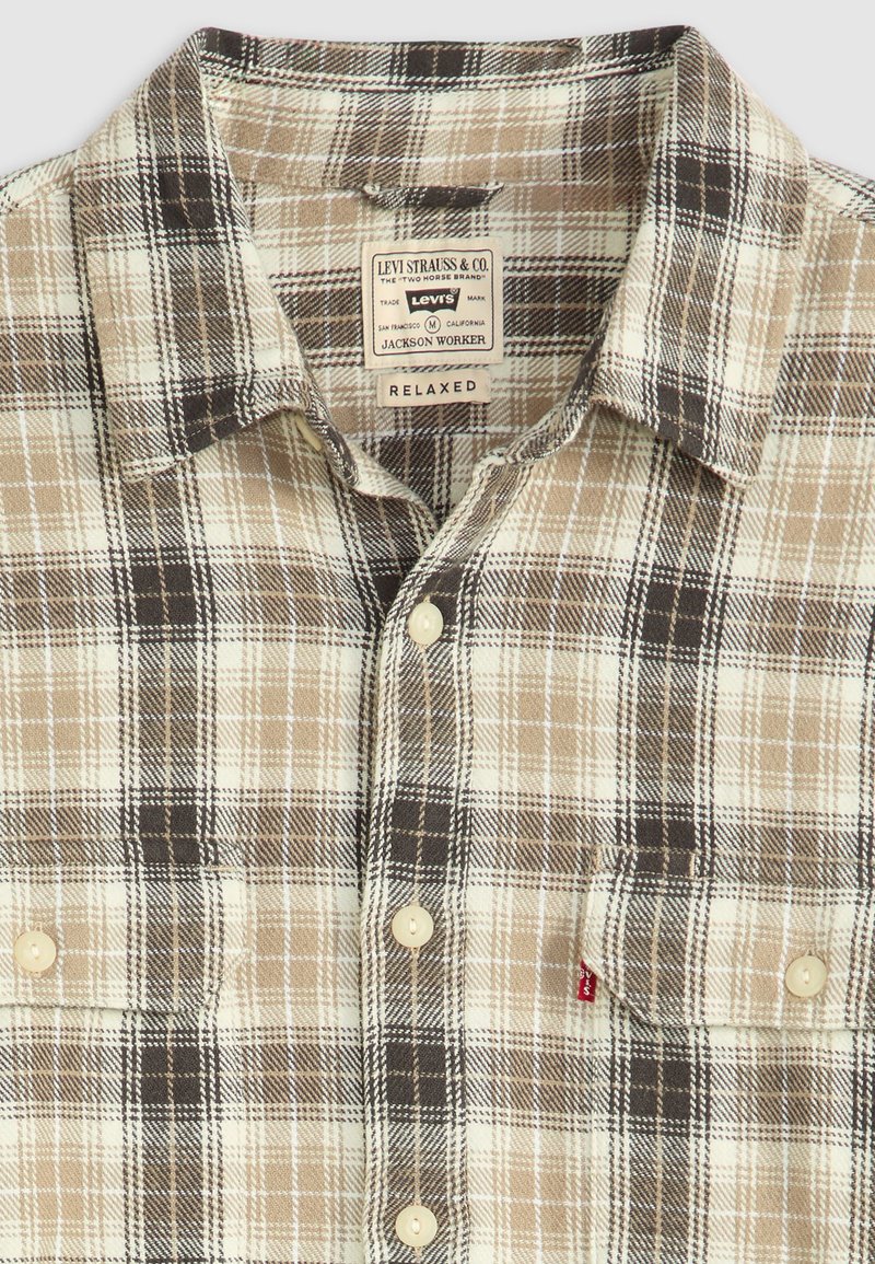 Plaid button-up shirt featuring brown, beige, and white colors. Cotton fabric, relaxed fit, with an emblem on the left pocket and beige buttons.