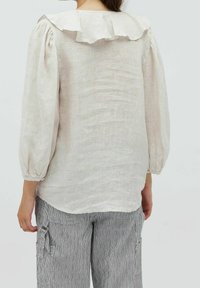 Blusa di lino beige chiaro con colletto arricciato, maniche a sbuffo arricciate e finitura testurizzata, abbinata a pantaloni grigi a righe.