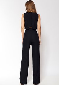 Czarny kombinezon z bezrękawnikowym topem, z zapięciem na guziki z tyłu oraz szerokimi spodniami. Wykonany z gładkiego materiału z dopasowaną talią.