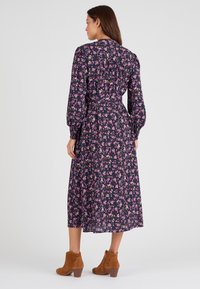 Vestido midi floral con una base de color púrpura oscuro, adornado con flores rosas y amarillas. Incluye mangas largas abullonadas y una cintura ceñida con cinturón. Botines de ante marrón hasta el tobillo.