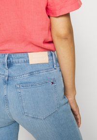 Jeans in denim azzurro con una toppa rosa con il marchio "TOMMY HILFIGER" sulla cintura e un piccolo logo decorativo sulla tasca posteriore.