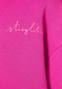 Fuchsiová mikina s žebrovanou texturou, na přední straně zdobená růžovým kurzívním vyšíváním slova "stieglitz".