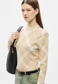 Bluza bej cu mâneci lungi și model în carouri albe. Croială strâmtă cu guler înalt. Asortată cu blugi verde deschis și o geantă neagră din piele.