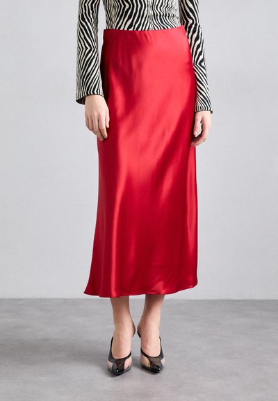 Jupe en satin rouge avec une texture lisse, présentant une coupe droite et une longueur cheville. Associée à des talons ouverts noirs.