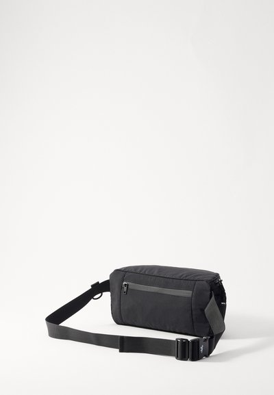 Sac messager en tissu noir de forme rectangulaire, avec une sangle ajustable, une poche zippée à l'avant et une surface texturée. Design compact et minimal.