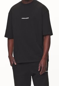 Svart bomullströja med korta ärmar och en avslappnad passform. Har en vit "PEGADOR" textlogotyp på bröstet. Enkel design med en ren silhuett.