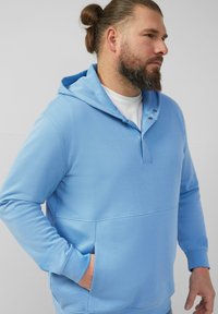 Hellblaues Kapuzenpullover mit strukturierter Oberfläche, ausgestattet mit einem halben Knopfleistenverschluss, einer Kängurutasche und gerippten Bündchen.