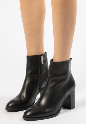 Bottes noires en cuir à chevilles avec un talon bloc haut et un bout pointu. Elles disposent d'une fermeture à zip sur le côté et d'une texture lisse.