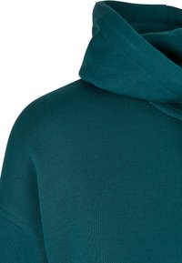 Teal kangast lähedalt vaadates, millel on tekstuurne viimistlus ja ümmargune kapuuts, millel on õrnad tikandi detailid.