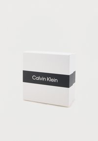 White box featuring a black band with "Calvin Klein" printed in white. Smooth texture with sharp edges. Simple and modern design.