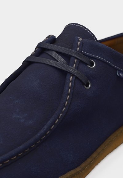 Μπλε ναυτικό καστόρινο casual παπούτσι με μαύρα κορδόνια, μπεζ ραφές κατά μήκος των άκρων, μεταλλικές οπές και ορατή καφέ σόλα.