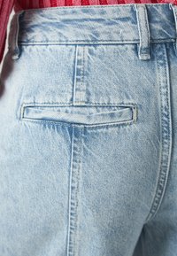 Lyseblå denimjeans med en baklomme med sydd klaff og en subtil slitt struktur på stoffet.