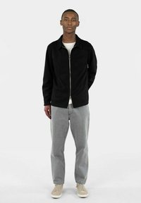 Sorte zip-up jakke laget av myk stoff, med en brystlomme; kombinert med lysegrå jeans og beige sneakers. Enkel, moderne design.