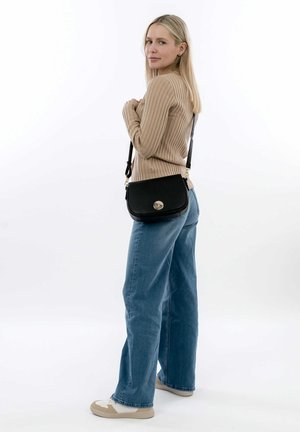 Black crossbody bag with a textured finish, gold hardware, and a circular closure. Worn with light blue flared jeans and a beige ribbed sweater.