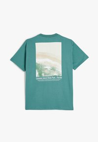 Camiseta de algodón color verde azulado con un estampado en la espalda del Parque Estatal de Caladesi Island, Florida, que incluye una ilustración del paisaje y detalles en texto blanco.