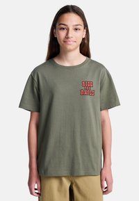 Camiseta de algodón verde oliva con mangas cortas, que presenta texto bordado en rojo "RIDE THE RAILS" en la zona del pecho izquierdo. Diseño simple.