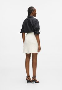 Fekete ing, felgöngyölt ujjak, fehér textúrájú mini szoknya és fekete pántos magassarkú cipő. Minimalista, testhez álló kialakítás; sima anyag kontrasztban van a részletes szoknyával.