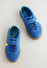 Blauwe suède sneakers met een geplatte bruine rubberen zool, voorzien van veters en klittenbandsluitingen, en neongele accenten op de hiel en zijkanten.