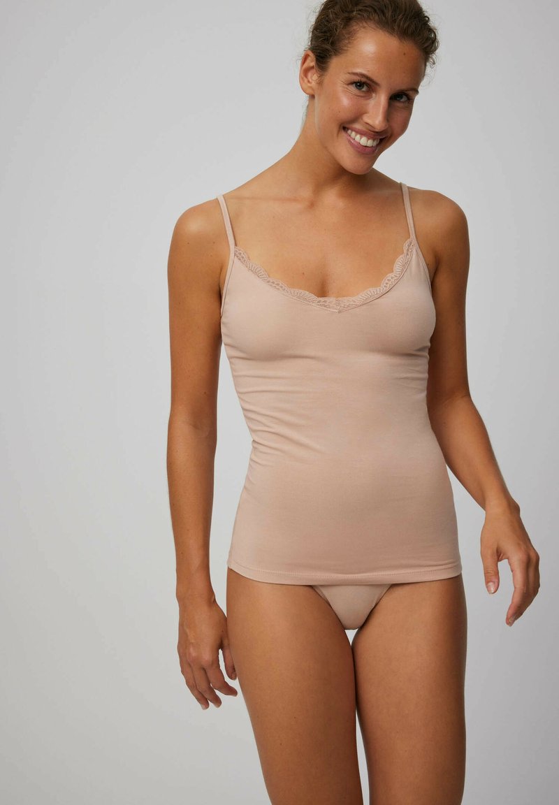 Camiseta nude sin mangas con tirantes ajustables, fabricada en un tejido suave y con un delicado encaje en el escote. Combinada con una braguita a juego.