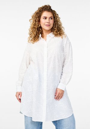 White button-up shirt with floral embroidery, long sleeves, and a relaxed fit, paired with light blue denim jeans.