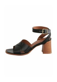 Schwarze Leder-Absatzsandalen mit Kreuzgurtdesign, offener Zehenpartie, Knöchelriemen mit goldener Schnalle und Holztextur-Absatz.