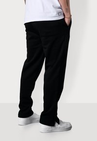 Schwarze Hose mit lockerer Passform, ausgestattet mit seitlichen Taschen und einem Kordelzugbund. Kombiniert mit weißen Turnschuhen, die ein sauberes Design zeigen.