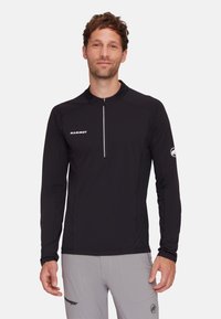 Schwarzes Langarmshirt mit einem Viertel-Reißverschluss-Kragen, das das "Mammut"-Logo auf der Brust und ein rundes Logo am Ärmel trägt. Glatte Textur.