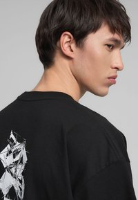 T-shirt nera in cotone con un design astratto bianco testurizzato sul retro, colletto rotondo e maniche corte.