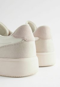 Sneaker bianche e rosa chiaro con una texture scamosciata sul tallone, caratterizzate da un corpo in pelle liscia e una suola in gomma spessa.