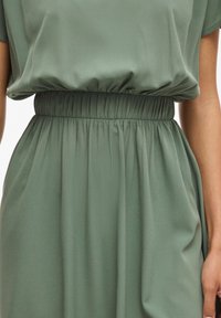 Vestido verde de tejido suave con un corte relajado, que presenta una cintura elástica y pliegues fluidos, ofreciendo una textura suave.