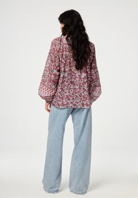 Vloeiende, bloemdessin blouse in tinten rood en paars, met een geplooide achterkant, lange mouwen en een zachte, lichte stof. Gecombineerd met losse, lichtblauwe jeans.