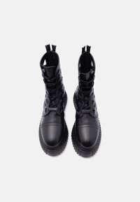 Paire de bottines noires à lacets avec semelles épaisses à rainures et côtés découpés, vues de dessus sur fond blanc.