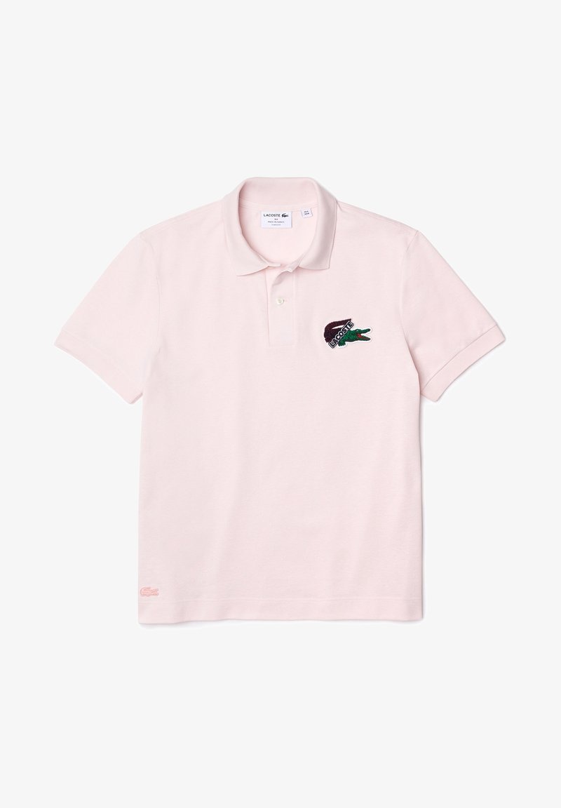 Polo rose clair à manches courtes avec col, patte de boutonnage et logo crocodile Lacoste brodé sur la poitrine gauche.